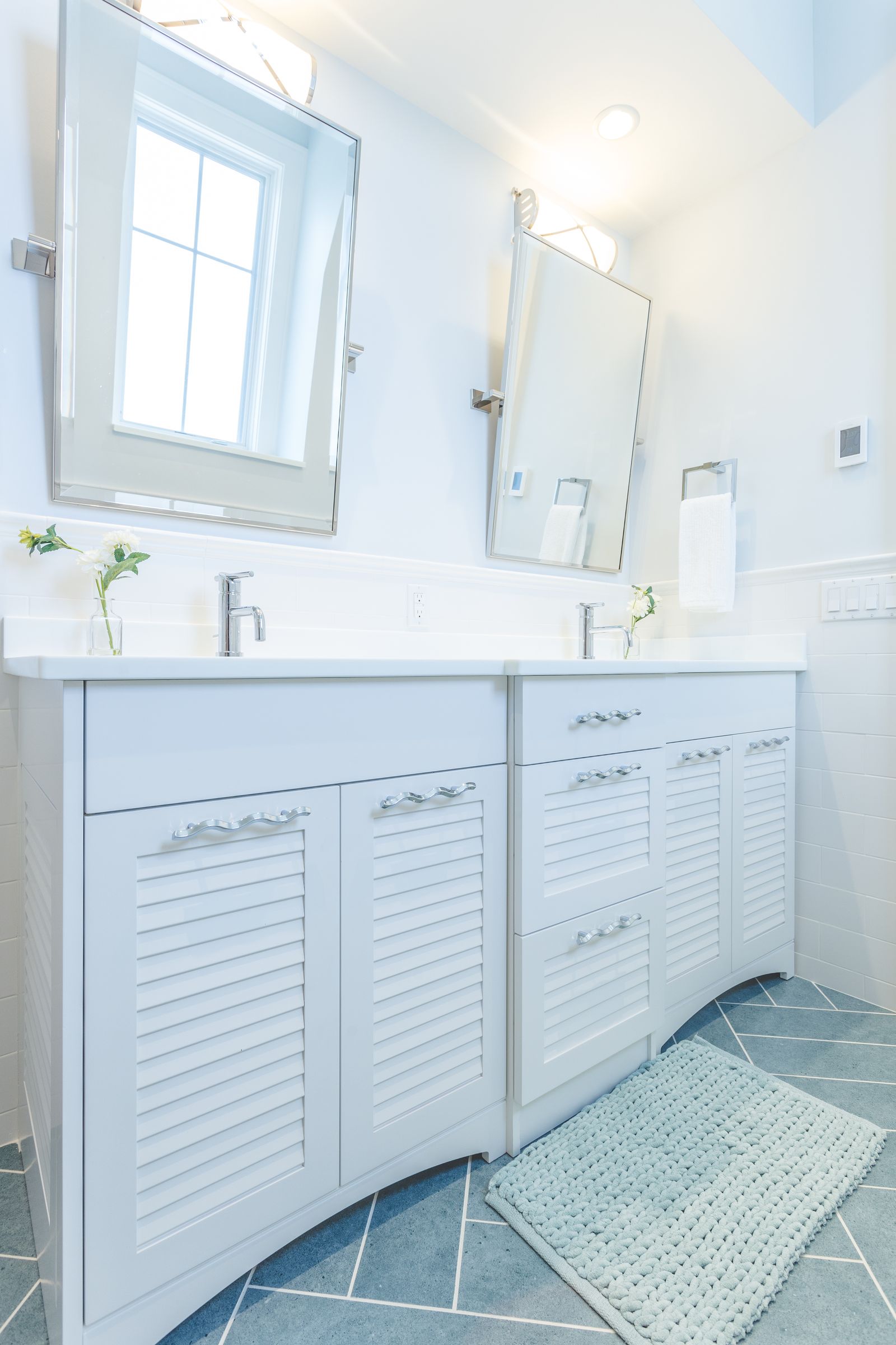 White double vanity with louvered doors on herringbone tile, built by Division Seven Millwork