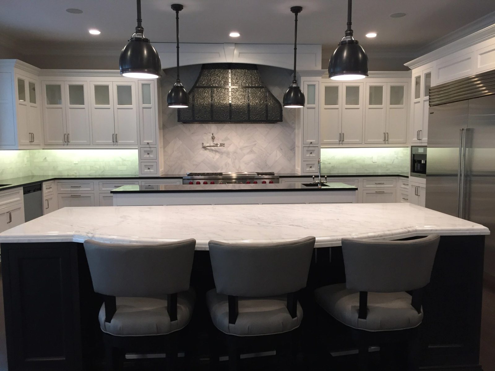 Custom white kitchen with marble island, herringbone marble backsplash, and a custom range hood built by Division Seven Millwork